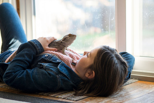 girl lying on the floor with a bearded dragon on her chest